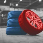 Stack of new tires and a red performance rim inside a professional garage, symbolizing growth, quality service, and the Rubens Tires Franchise Opportunity in the auto industry.